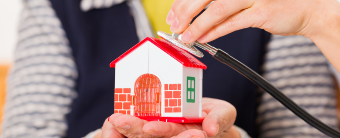 A senior woman holds a house in her hand as someone holds a stethoscope to it, symbolizing home care.