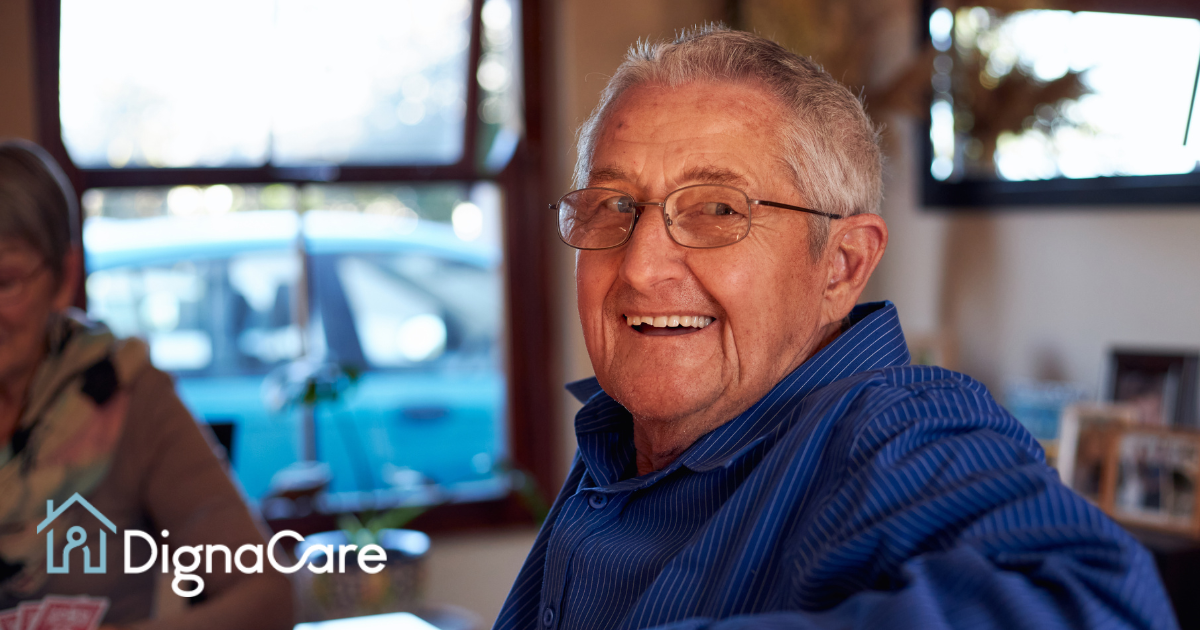 Smiling senior man, sitting at a table, enjoys aging in place at home as a result of successful long-distance caregiving.